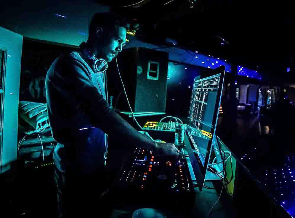 DJ Macalister Park performing live, illuminated by neon lights, surrounded by music production gear and digital mixing software.